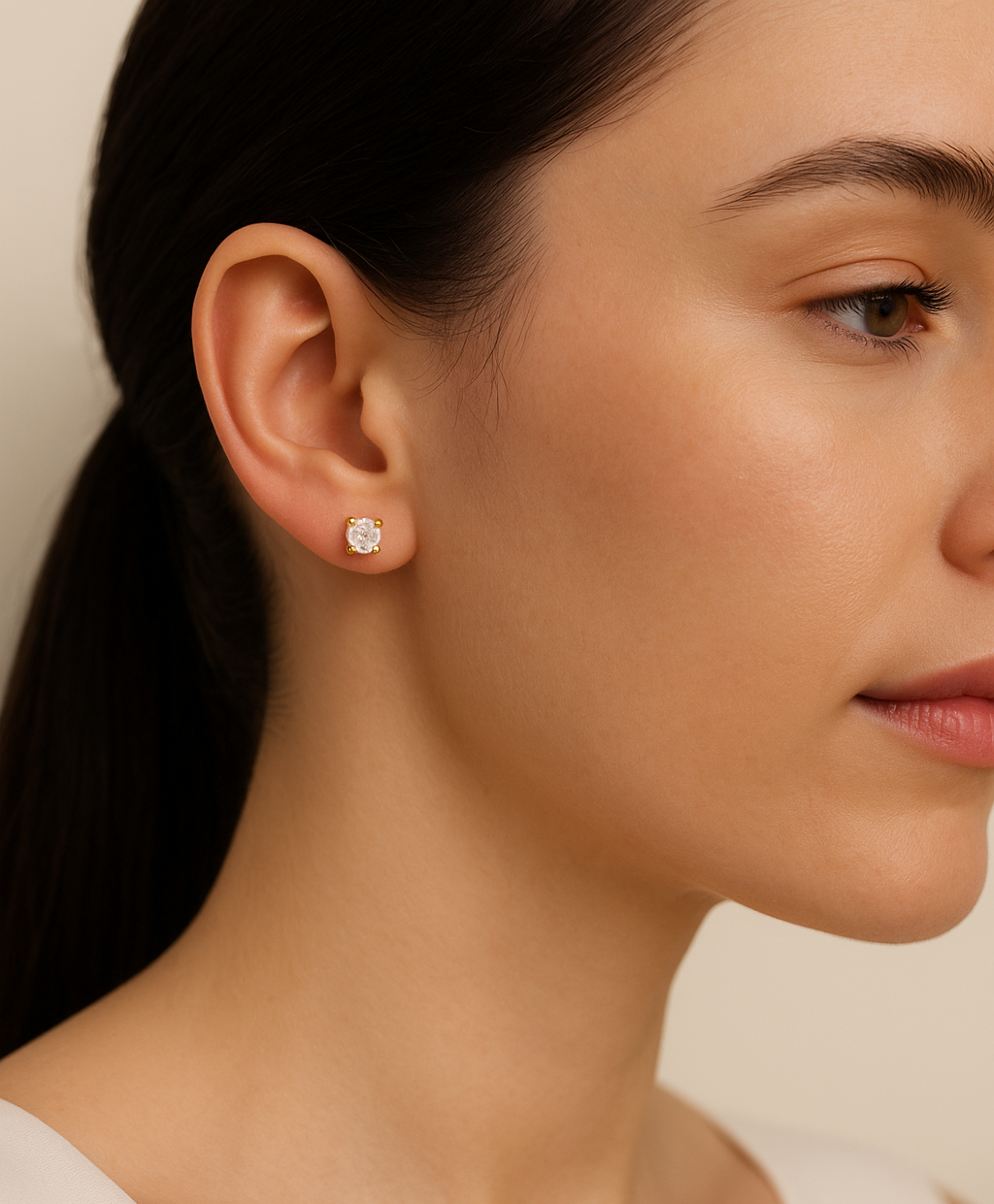 Close-up of a woman wearing diamond stud earrings with a neutral background