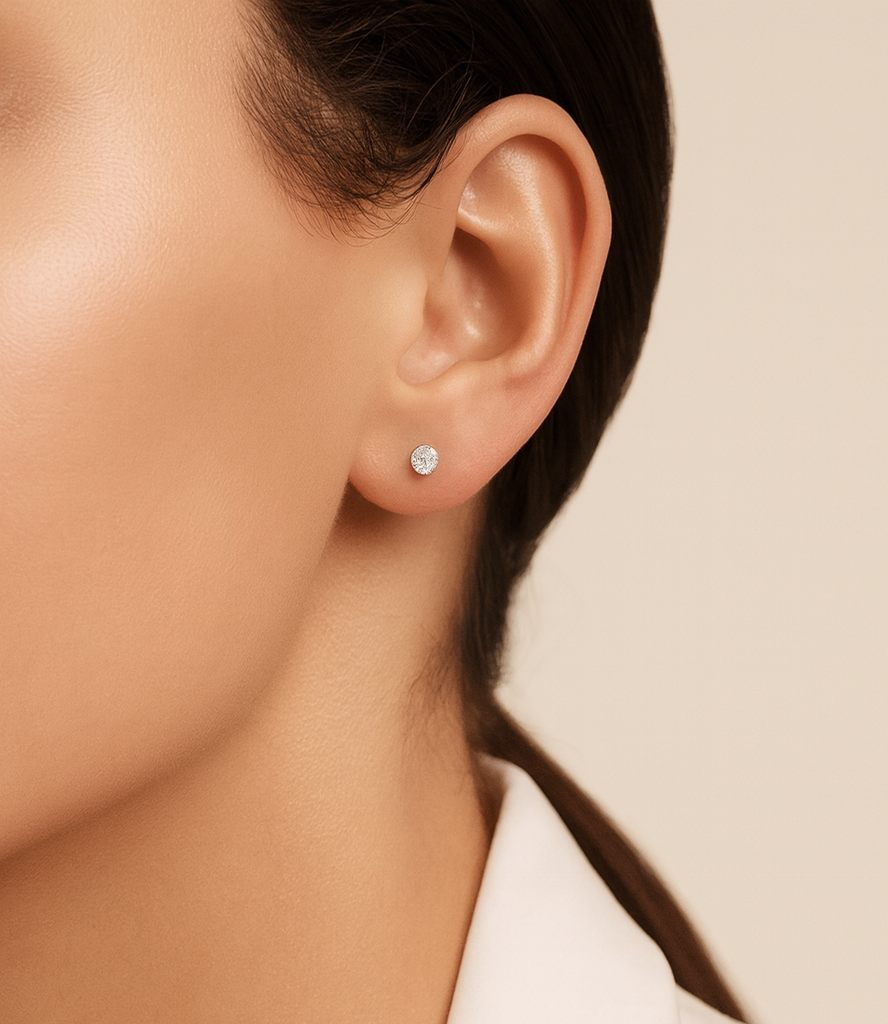 Close-up of an ear wearing a diamond stud earring on a neutral background