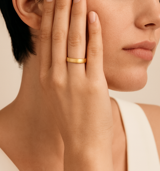 Close-up of a woman's hand with a gold ring on her finger, touching her face against a neutral background.