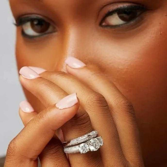 Close-up of a hand with pink nail polish wearing a diamond ring on a neutral background
