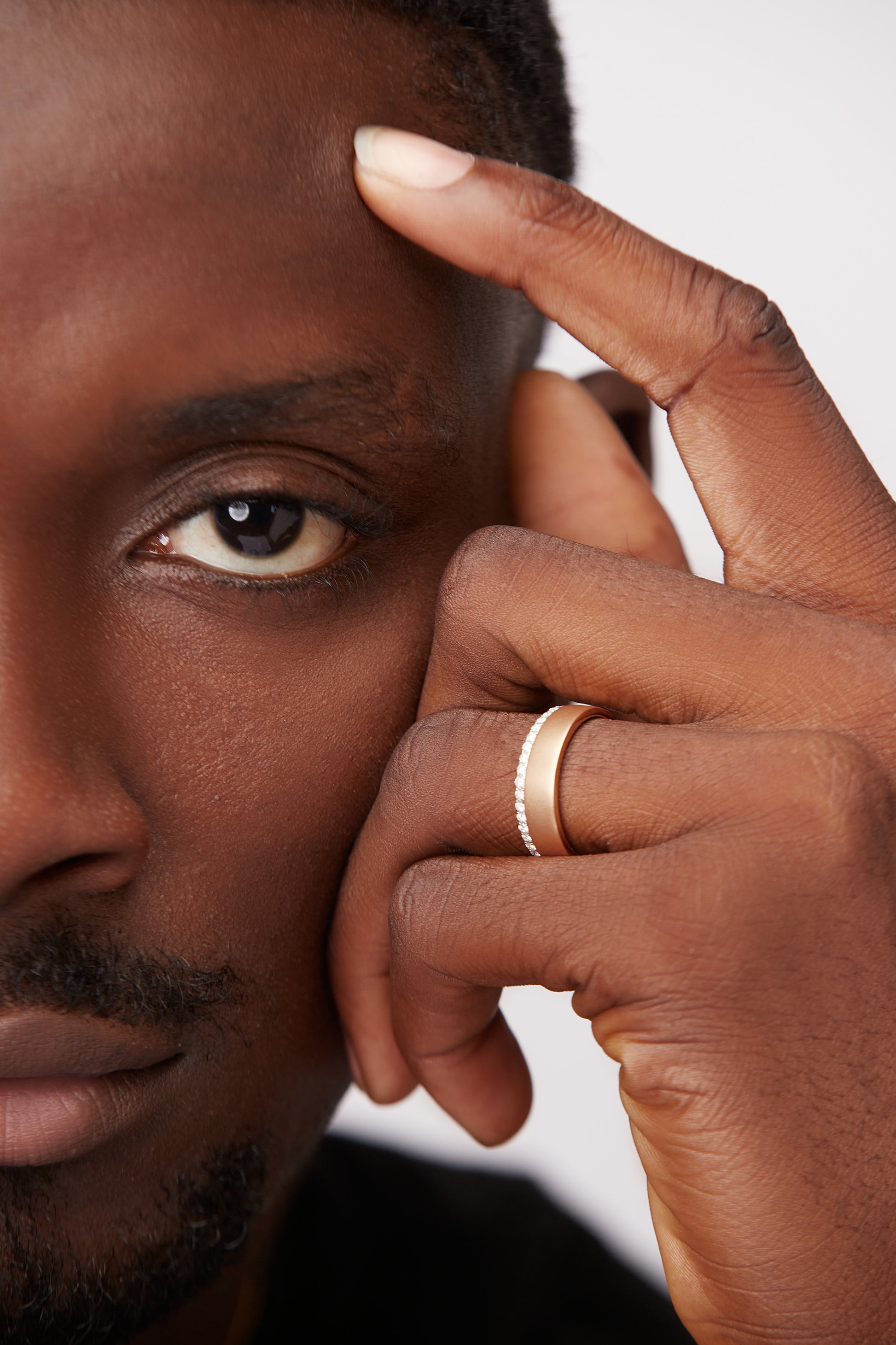 A man's hand featuring a 18K gold ring with natural diamond band on the ring finger.