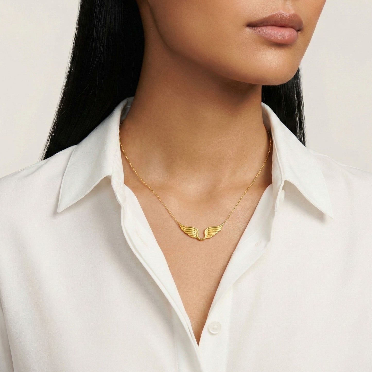 Gold wing-shaped necklace worn by a person in a white shirt