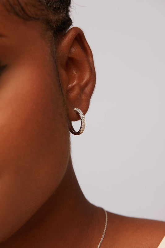 A close-up image of a person wearing a pair of hoop earrings with moissanite stones, made from 925 sterling silver.