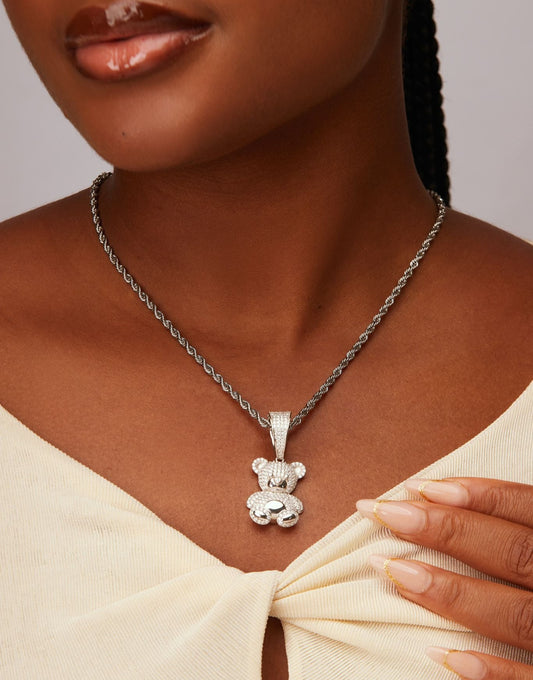 Silver teddy bear pendant necklace on a person wearing a beige top.