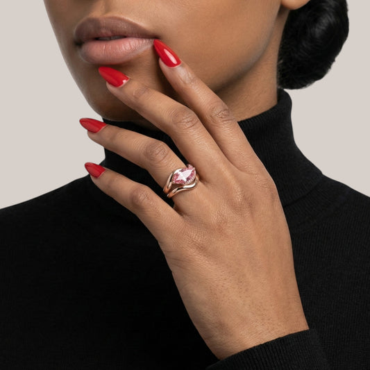 Hand with red nail polish wearing a pink ring on a neutral background