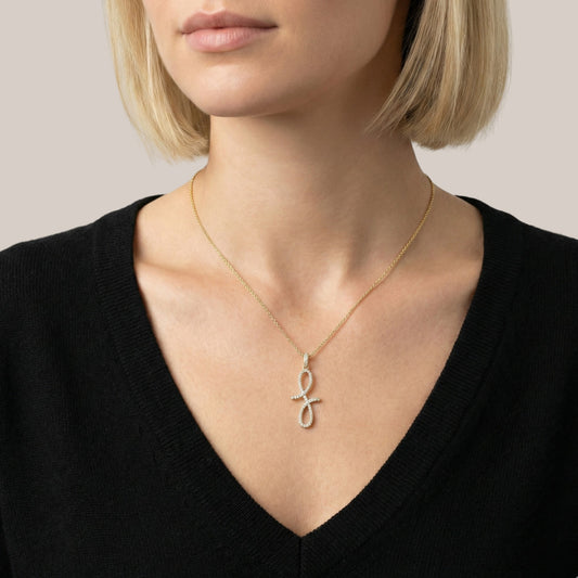 Woman wearing a gold necklace with a unique pendant against a neutral background