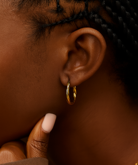 Close-up of an ear wearing a gold hoop earring with a blurred background