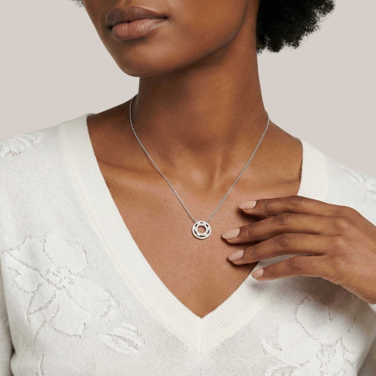 Woman wearing a silver necklace with a circular pendant on a neutral background