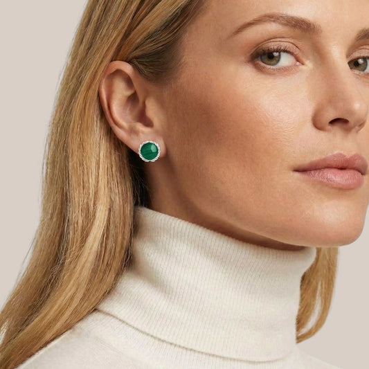 Close-up of a woman wearing green gemstone earrings with a neutral background