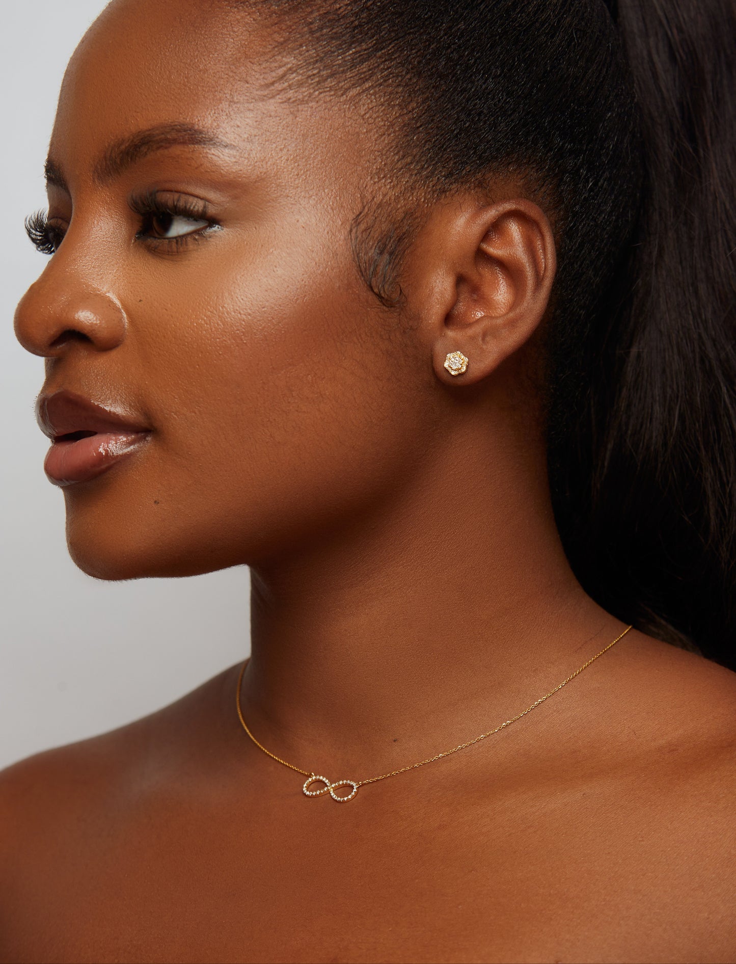 Woman wearing a gold necklace with an infinity symbol on a plain background