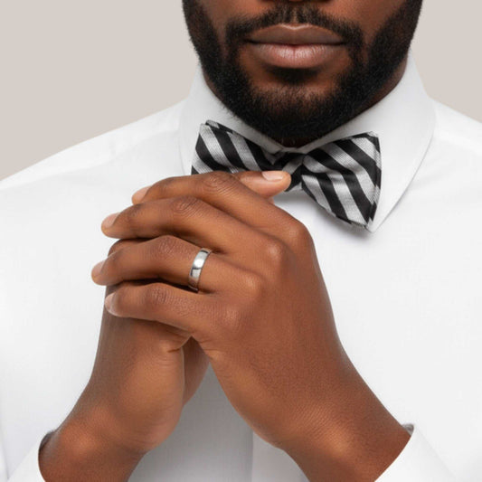 Man wearing a white shirt with a black and white striped bow tie, clasping his hands together.