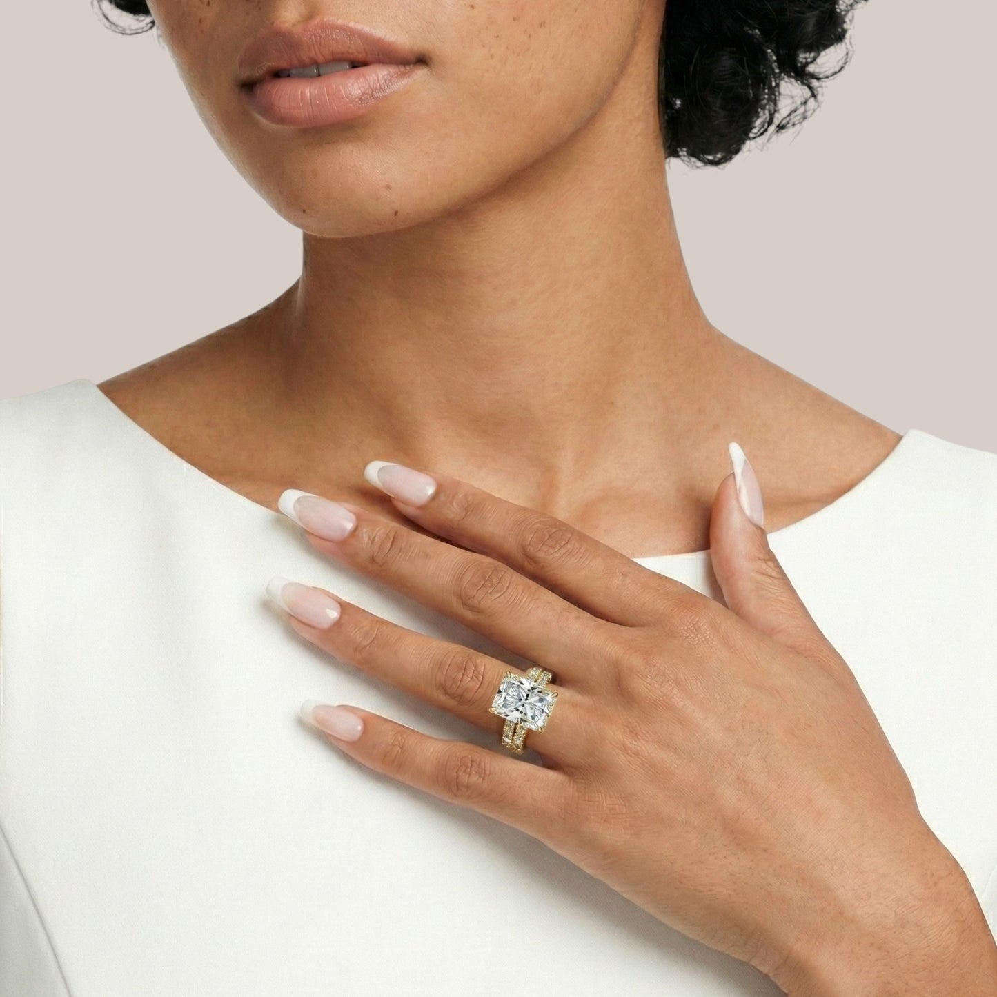 Woman wearing a gold ring with a diamond on a plain background