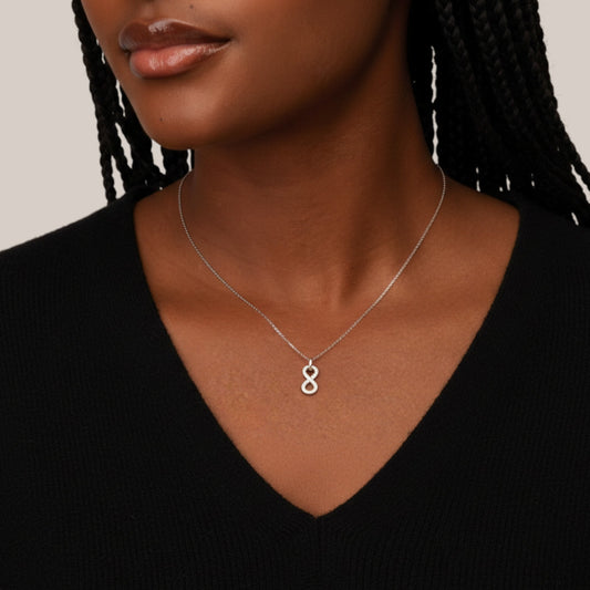 Woman wearing a silver necklace with an infinity symbol pendant on a neutral background