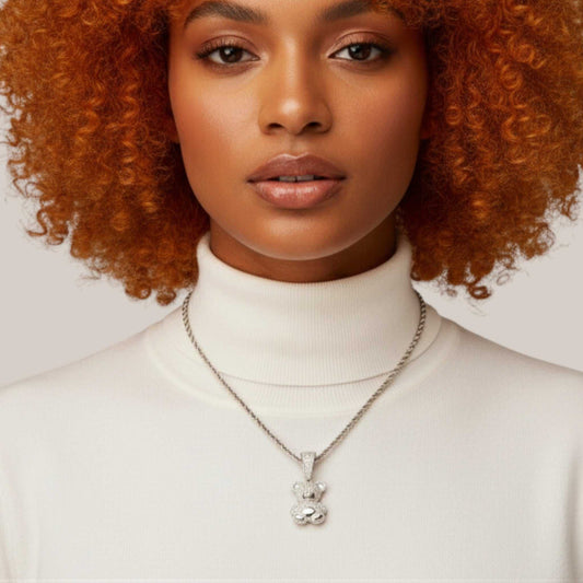 Woman wearing a white turtleneck and silver necklace with a pendant against a neutral background