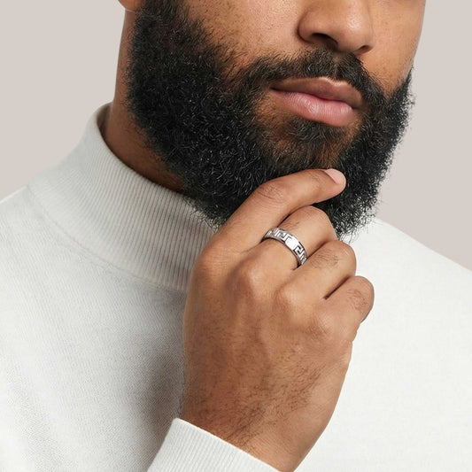Man wearing a silver ring on his finger, touching his beard against a neutral background