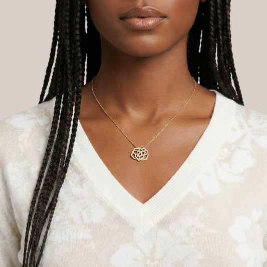 Woman wearing a gold necklace with a white sweater on a neutral background