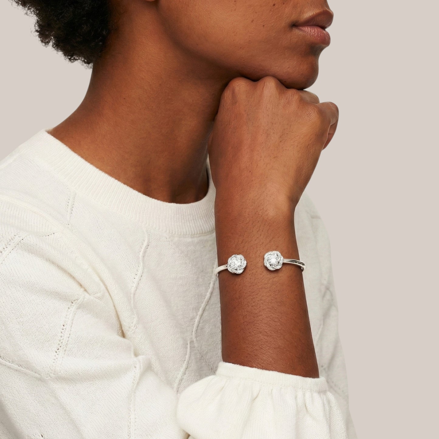 Person wearing a silver bracelet with two clear stones on a neutral background