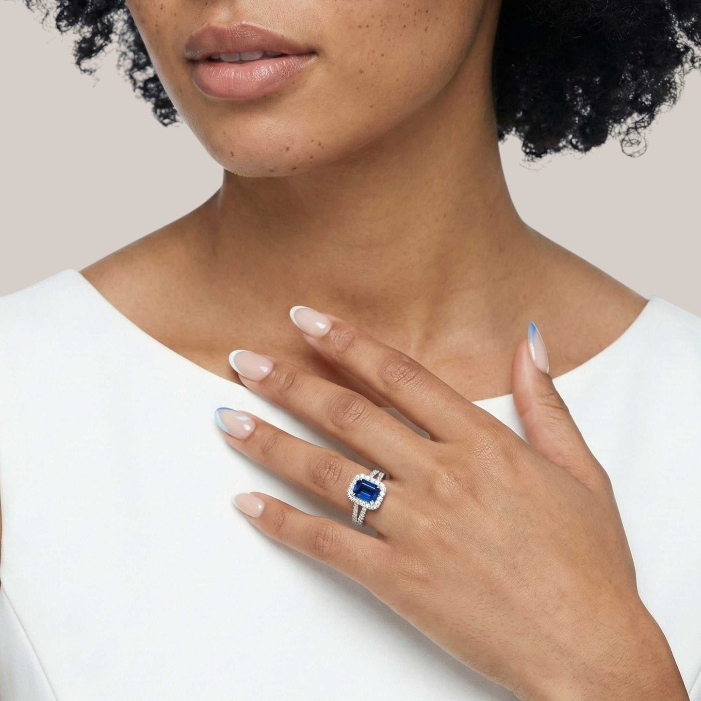 Woman wearing a ring with a blue gemstone on a plain background