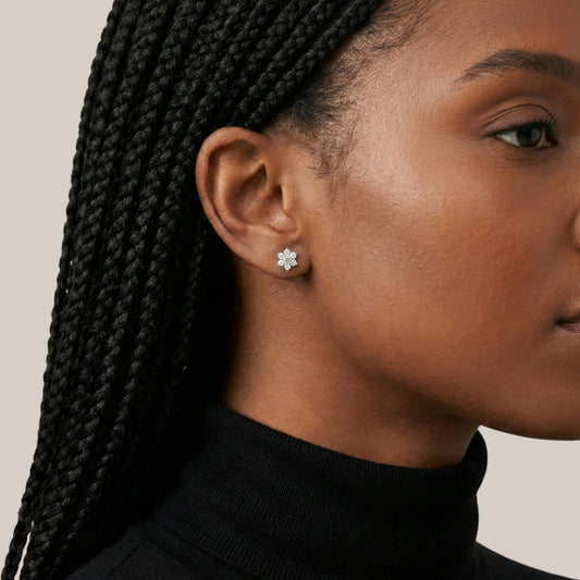 Close-up of a woman wearing diamond stud earrings with a neutral background