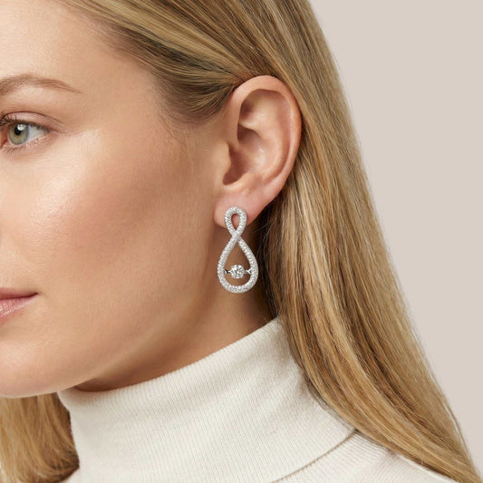 Close-up of a woman wearing a silver earring with a clear gemstone on a neutral background