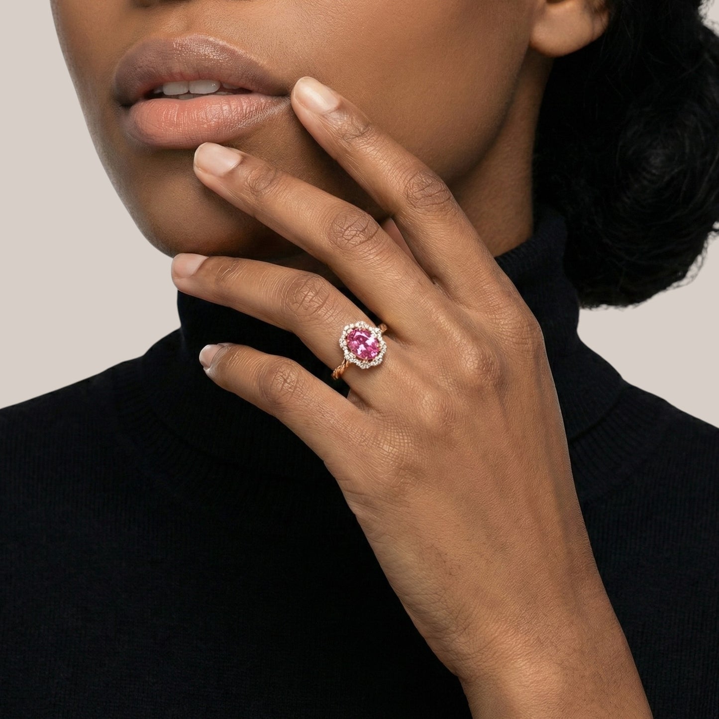 Close-up of a hand wearing a pink gemstone ring on a neutral background
