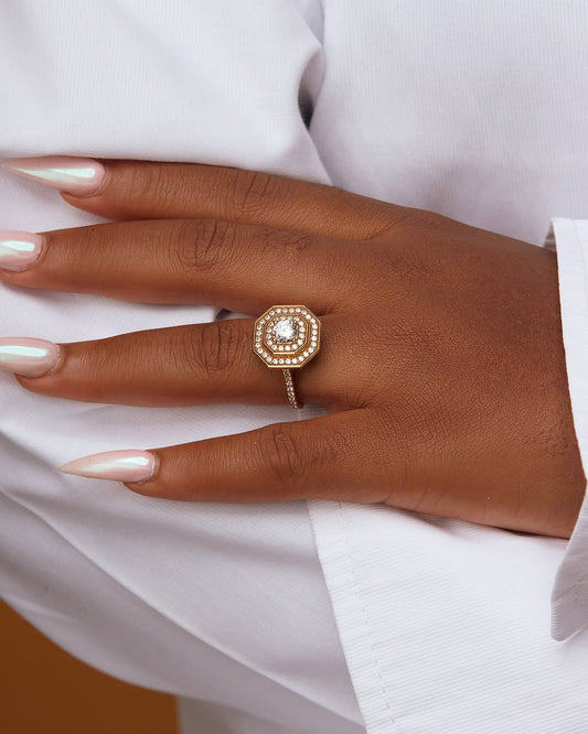 A close-up of a person's hand wearing a gold ring with a large central cubic zirconia stone, surrounded by smaller stones on the band.