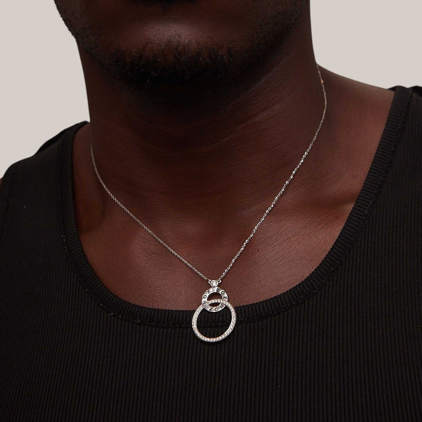 Silver necklace with a double ring pendant on a person wearing a black shirt.