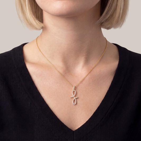 A close-up of a model wearing a delicate gold chain necklace with a small infinity symbol pendant set with tiny clear stones, paired with a black V-neck top.