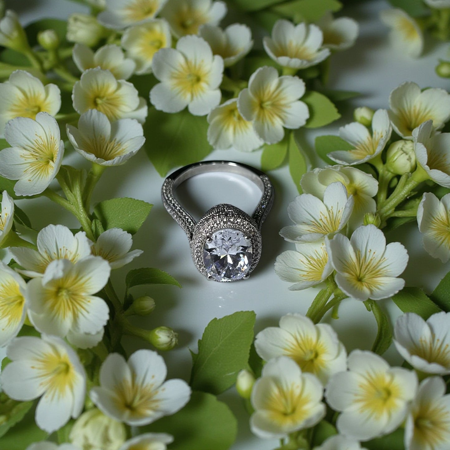 Silver ring with a large gemstone surrounded by white flowers and green leaves