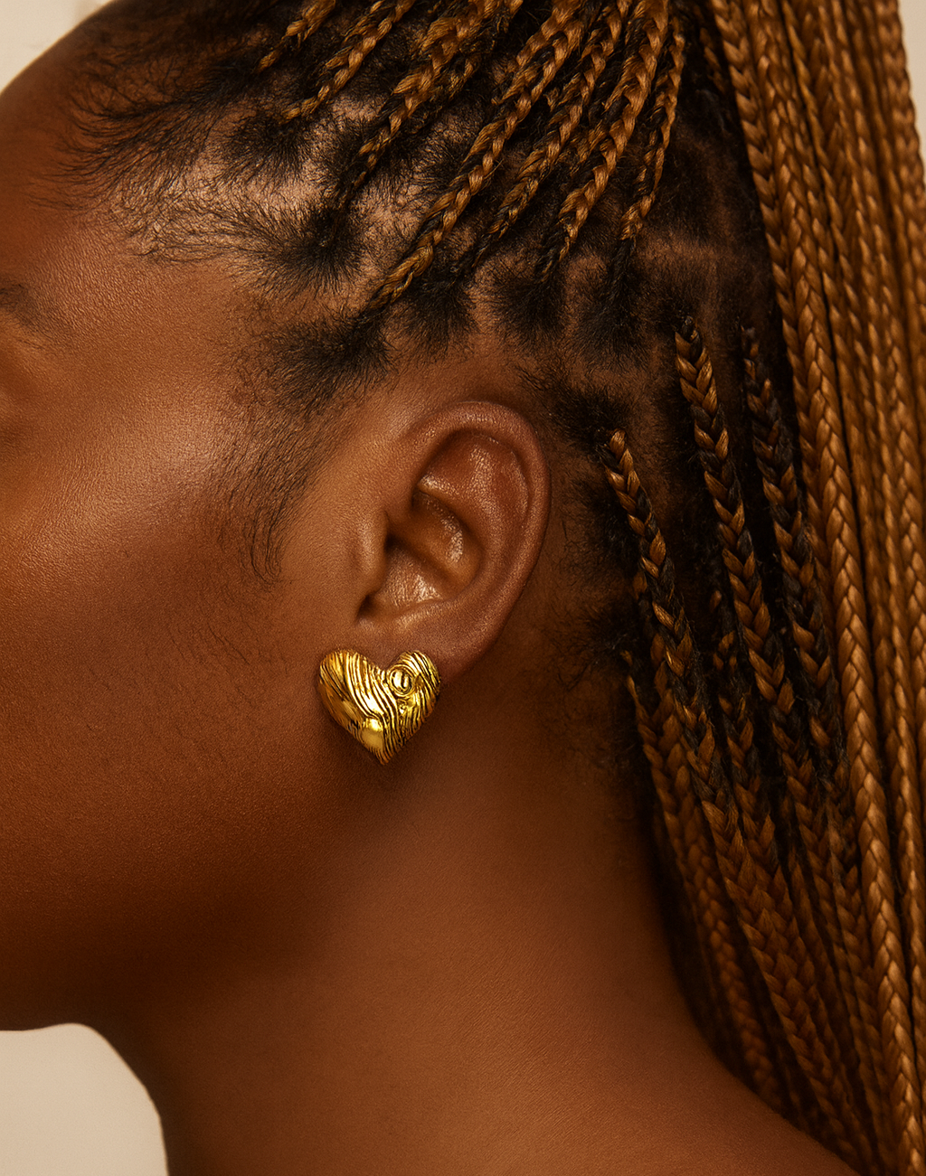 Close-up of an ear wearing a gold heart-shaped earring with braided hair.