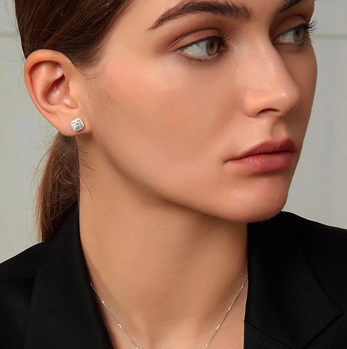 Close-up of a woman wearing diamond earrings with a neutral background