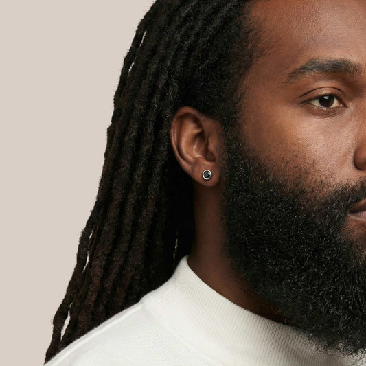 Close-up of a man with dreadlocks and a beard wearing a white shirt against a beige background