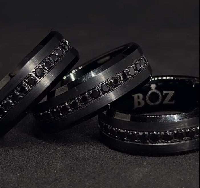 Two tungsten carbide bands with black sapphire accents, one with the inside of the band visible showing the sapphires, the other showing the outside with the word 'BOZ' on the band.