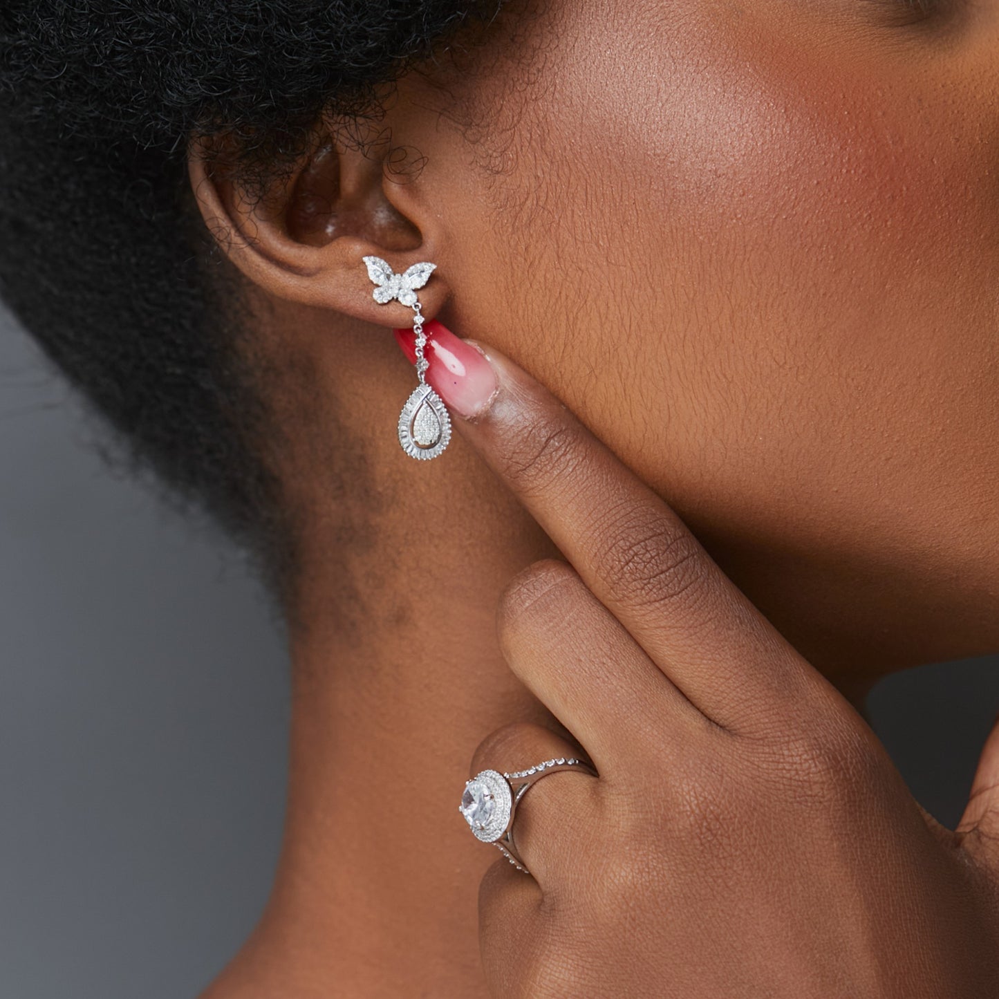 Close-up of a person wearing a butterfly-shaped earring and a ring on a neutral background