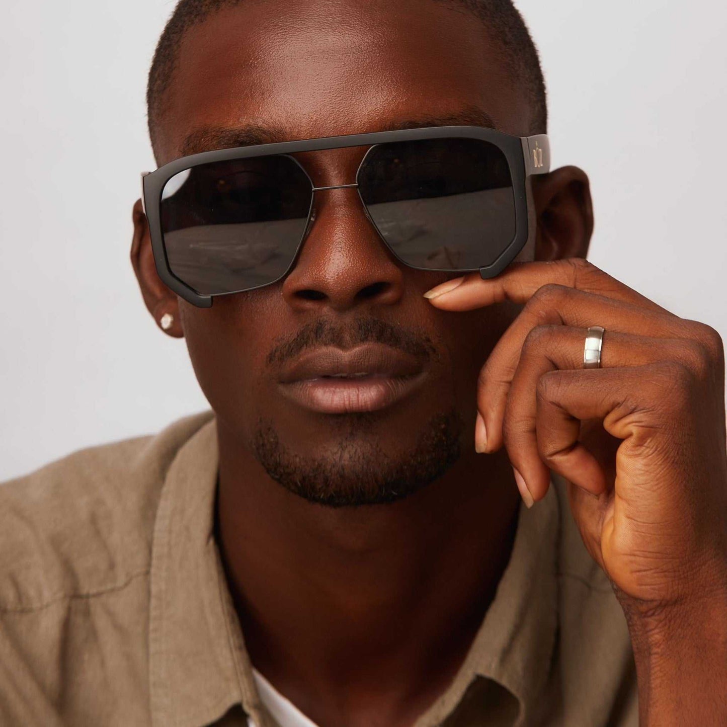 Man wearing sunglasses with one hand on a neutral background