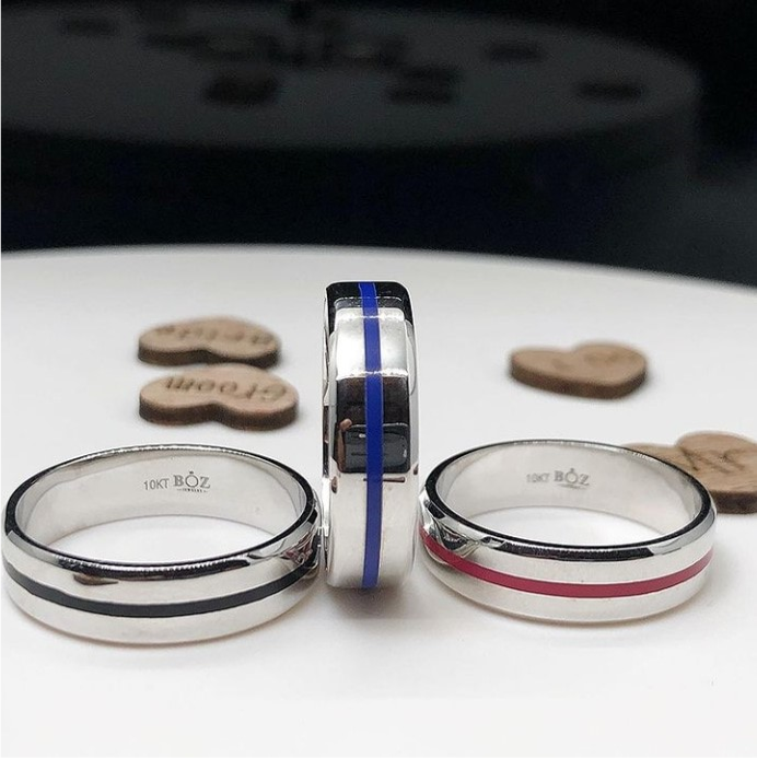 Two men's diamond rings with enamel lines, one in silver and one in gold color, displayed on a white surface, surrounded by small wooden discs.