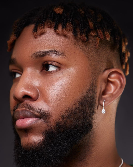 A close-up image of a man's face, focusing on his ear which features an earring with a small diamond.