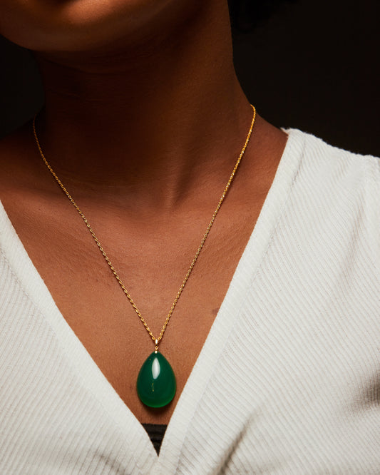 A person wearing a gold-colored necklace with a green pendant.