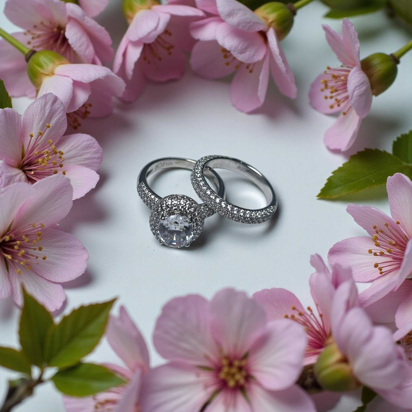 Zara Oval Cut CZ bride set in 925 sterling silver with oval cubic zirconia surrounded by halo and matching band among pink flowers