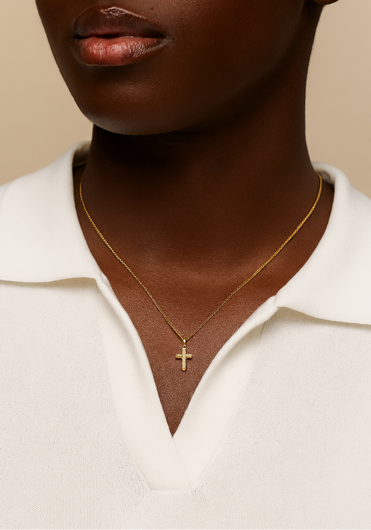 Close-up of a person wearing a gold necklace with a cross pendant on a beige background
