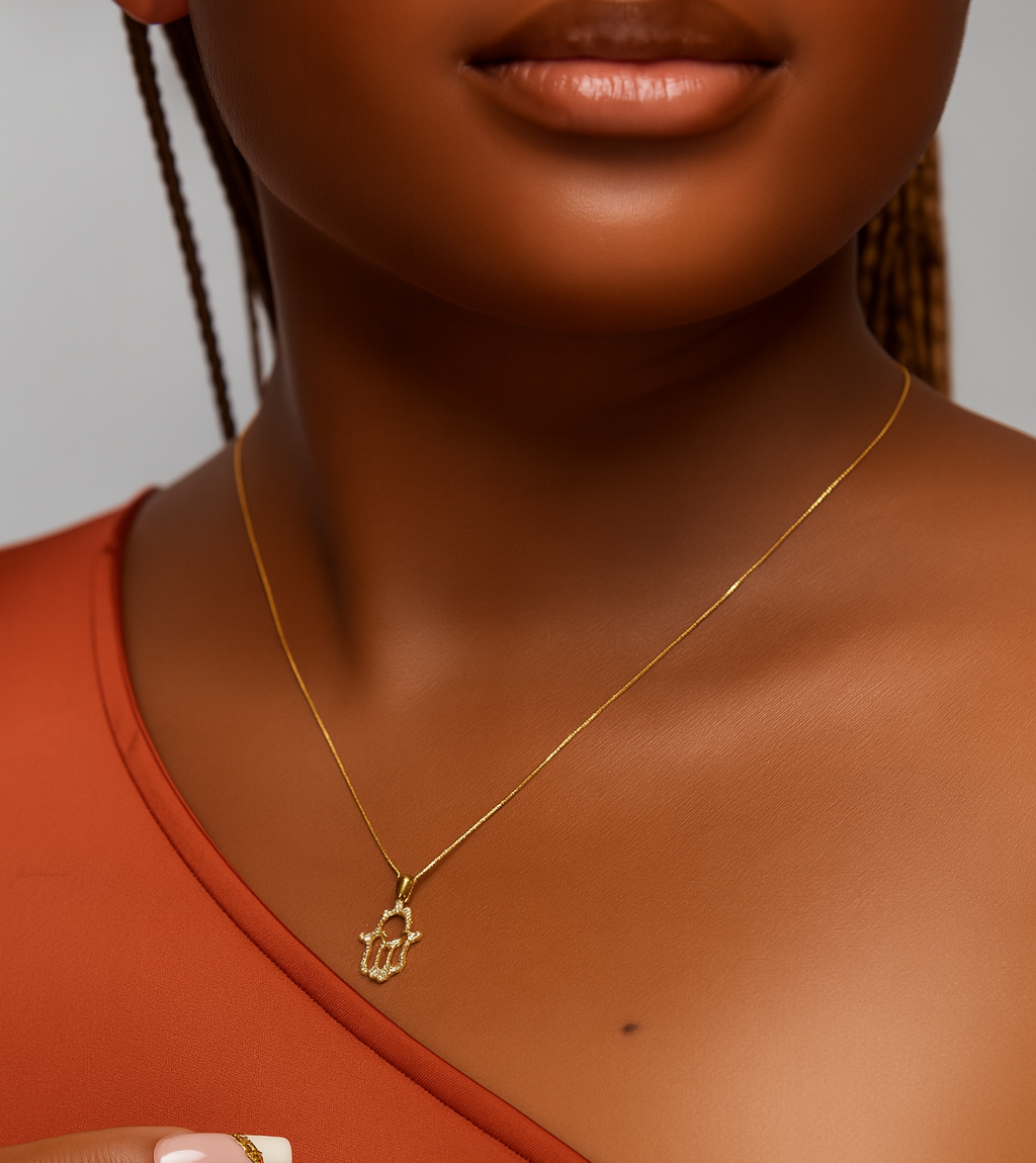 Close-up of a person wearing a gold necklace with a hamsa hand pendant.