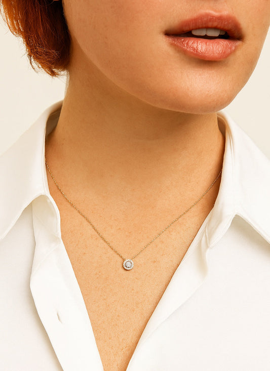 Close-up of a person wearing a delicate necklace with a small pendant on a plain background