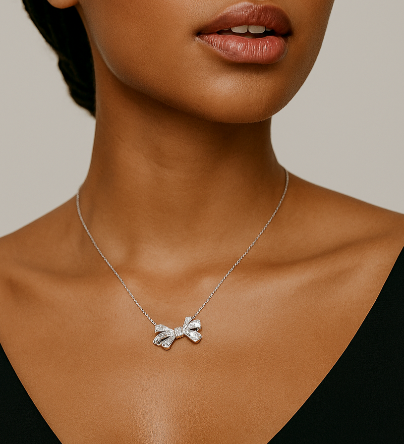 Woman wearing a silver necklace with a bow pendant against a neutral background