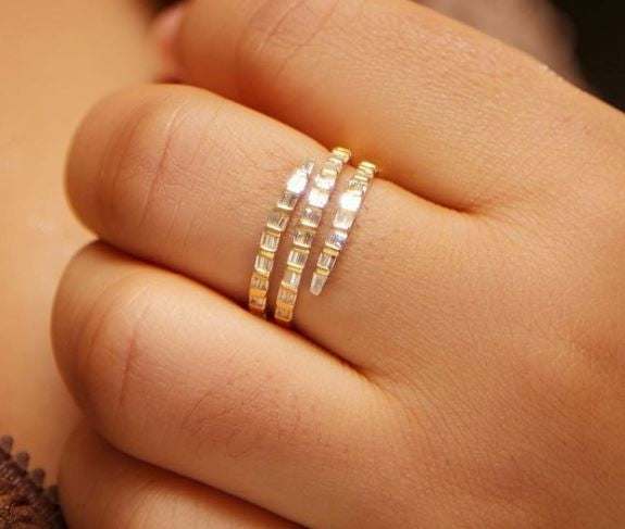 Close-up of a hand wearing an 18K gold Spiral Baguette Cut Moissanite Band with radiant baguette-cut stones in a spiral design
