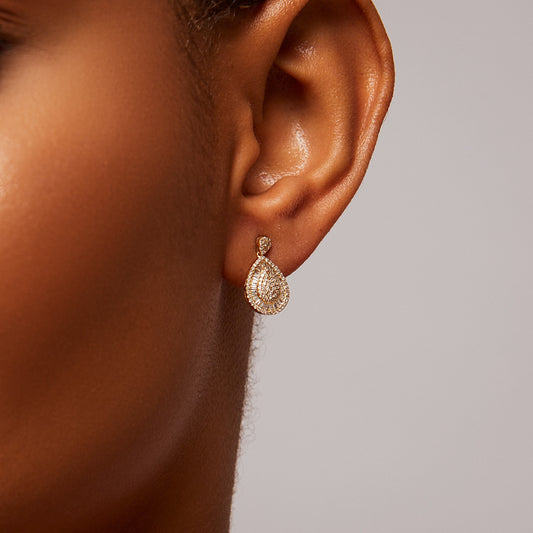 Gold teardrop earring worn on an ear with a neutral background