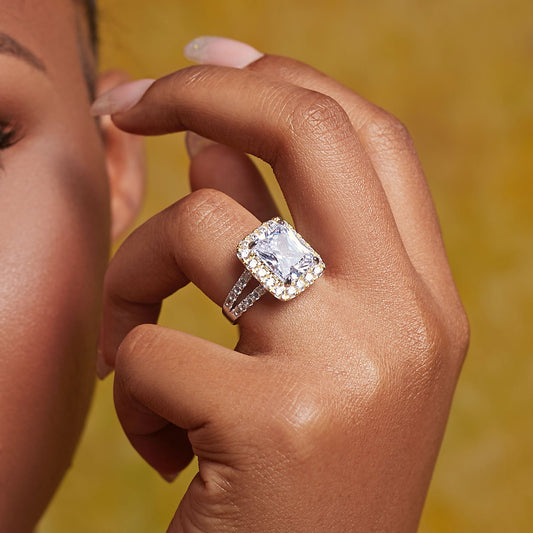 Close-up of a hand wearing a diamond ring with a blurred yellow background