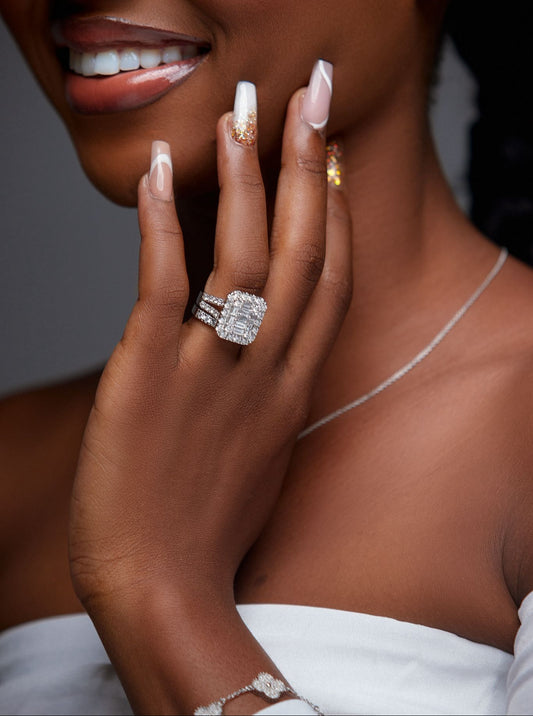 Close-up of a woman's hand with a diamond ring, white nail polish, and a blurred background.