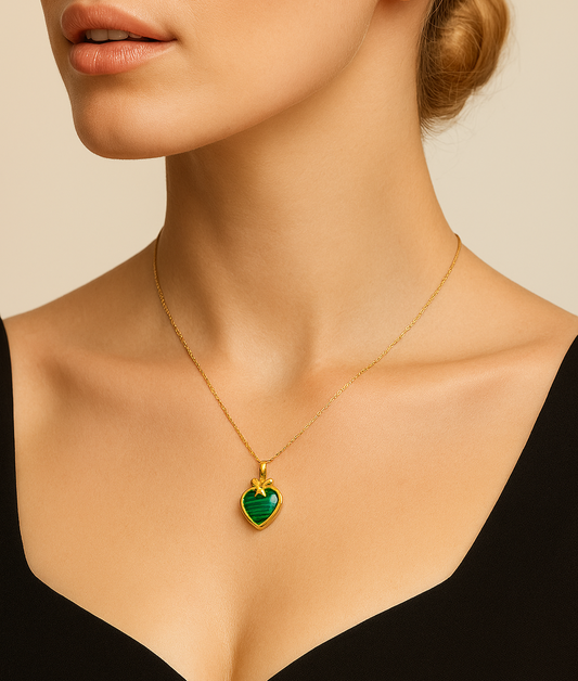 Woman wearing a gold necklace with a green heart pendant against a neutral background