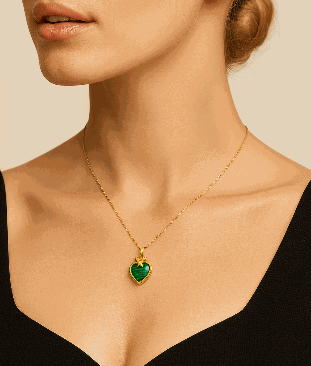 Woman wearing a gold necklace with a green heart pendant against a neutral background