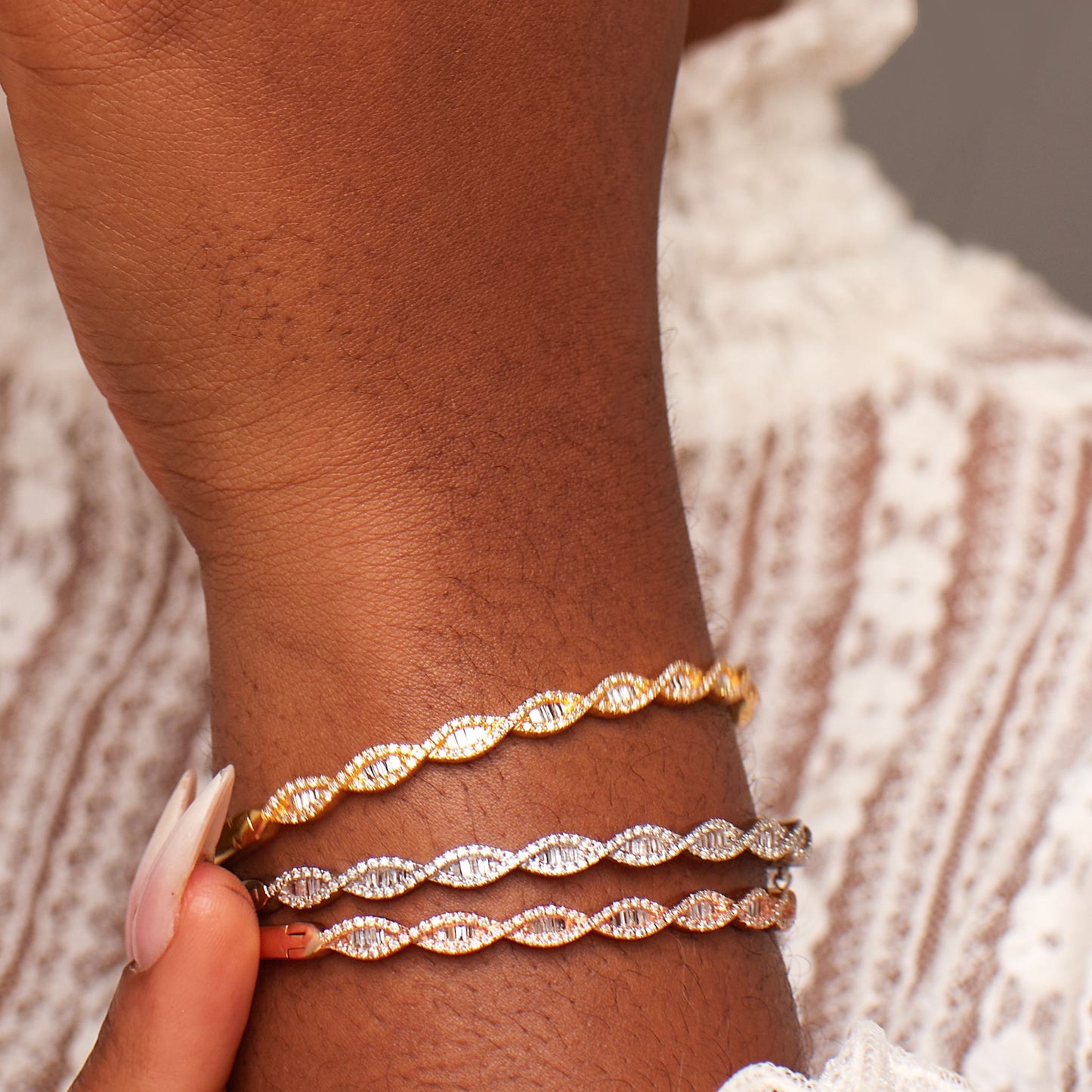 Close-up of a wrist wearing multiple gold bracelets on a textured fabric background
